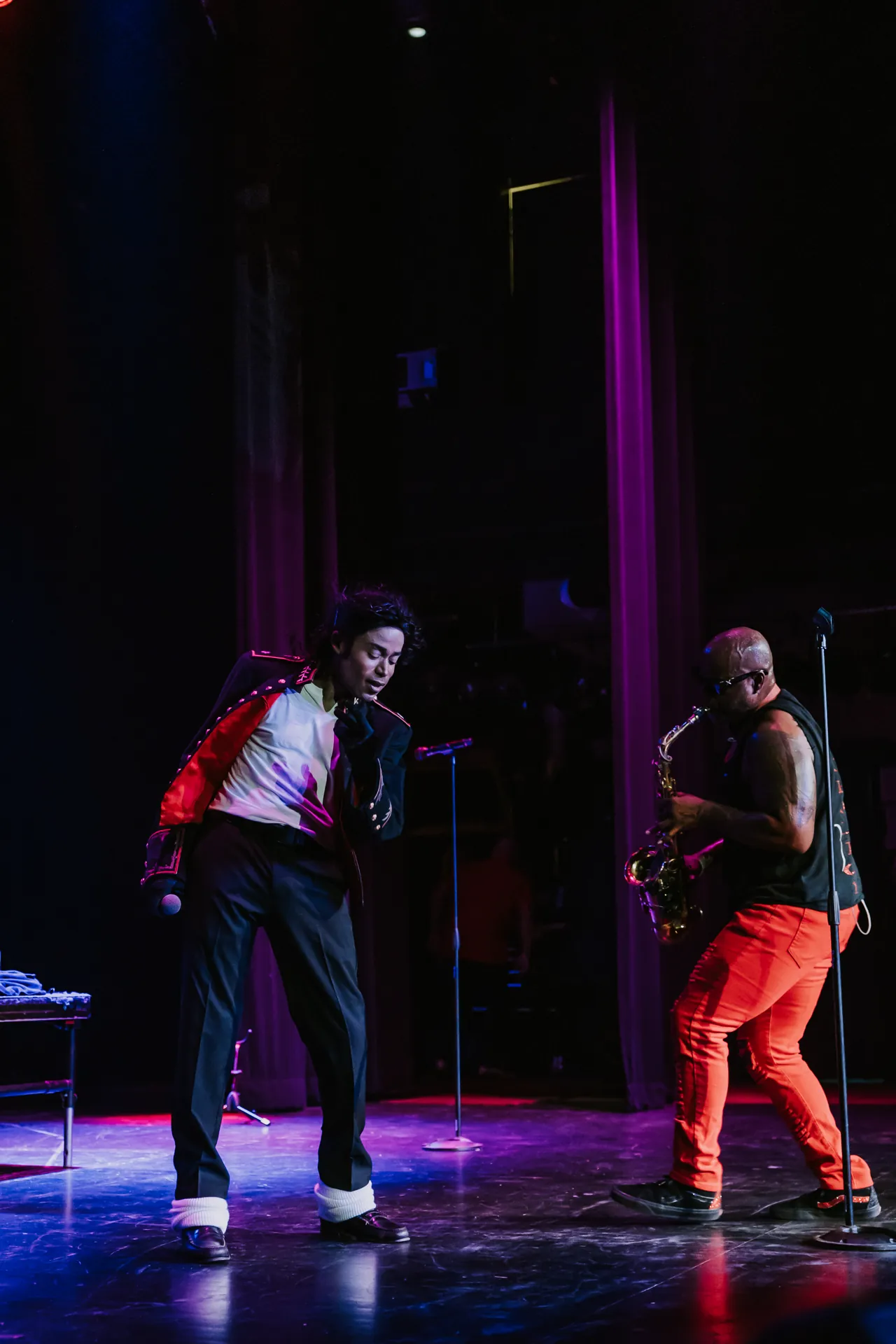 Two Who’s Bad performers in red and black dance in dramatic stage lighting