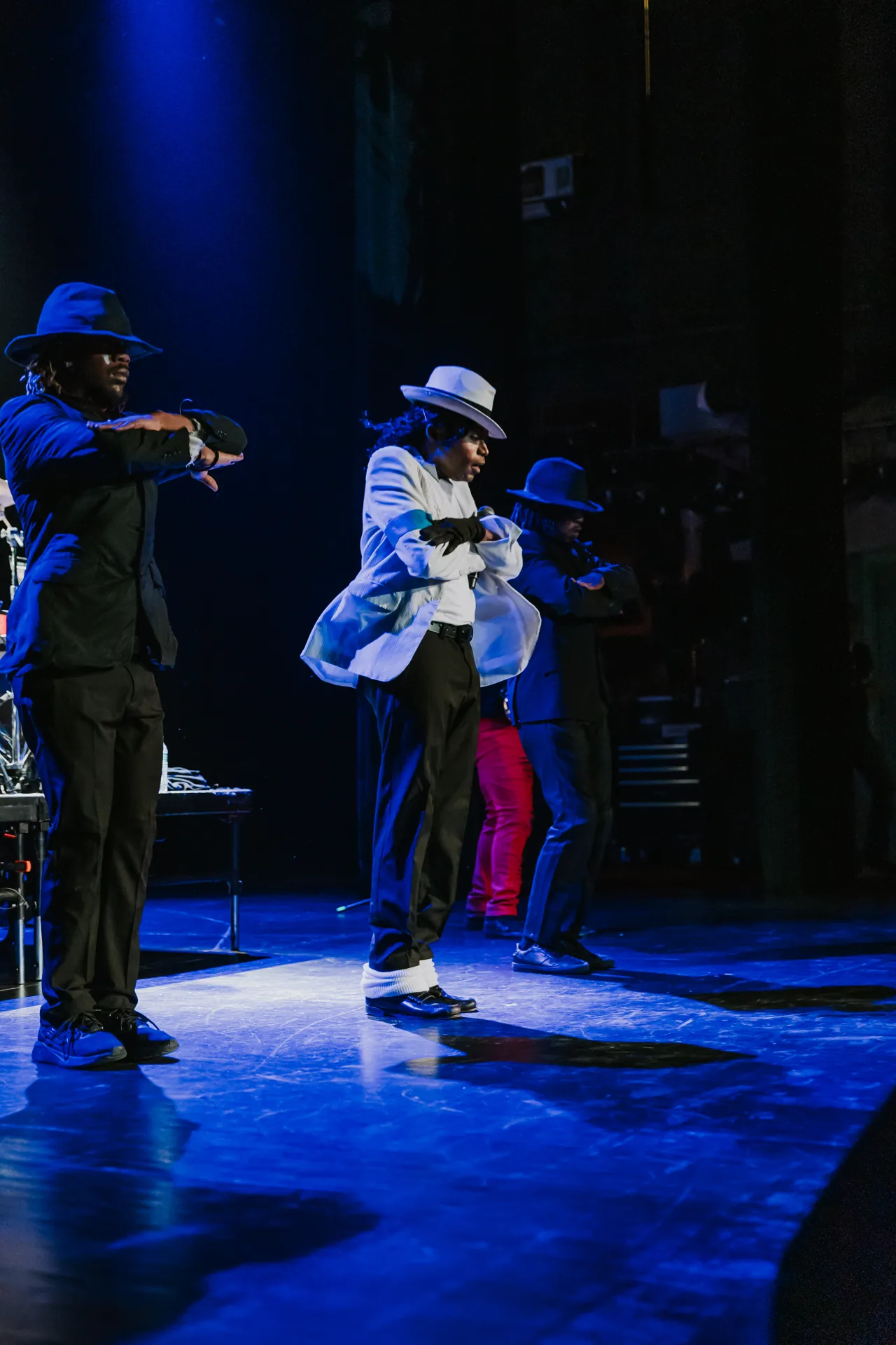 Two Who’s Bad performers in fedoras dance together on a blue-lit stage