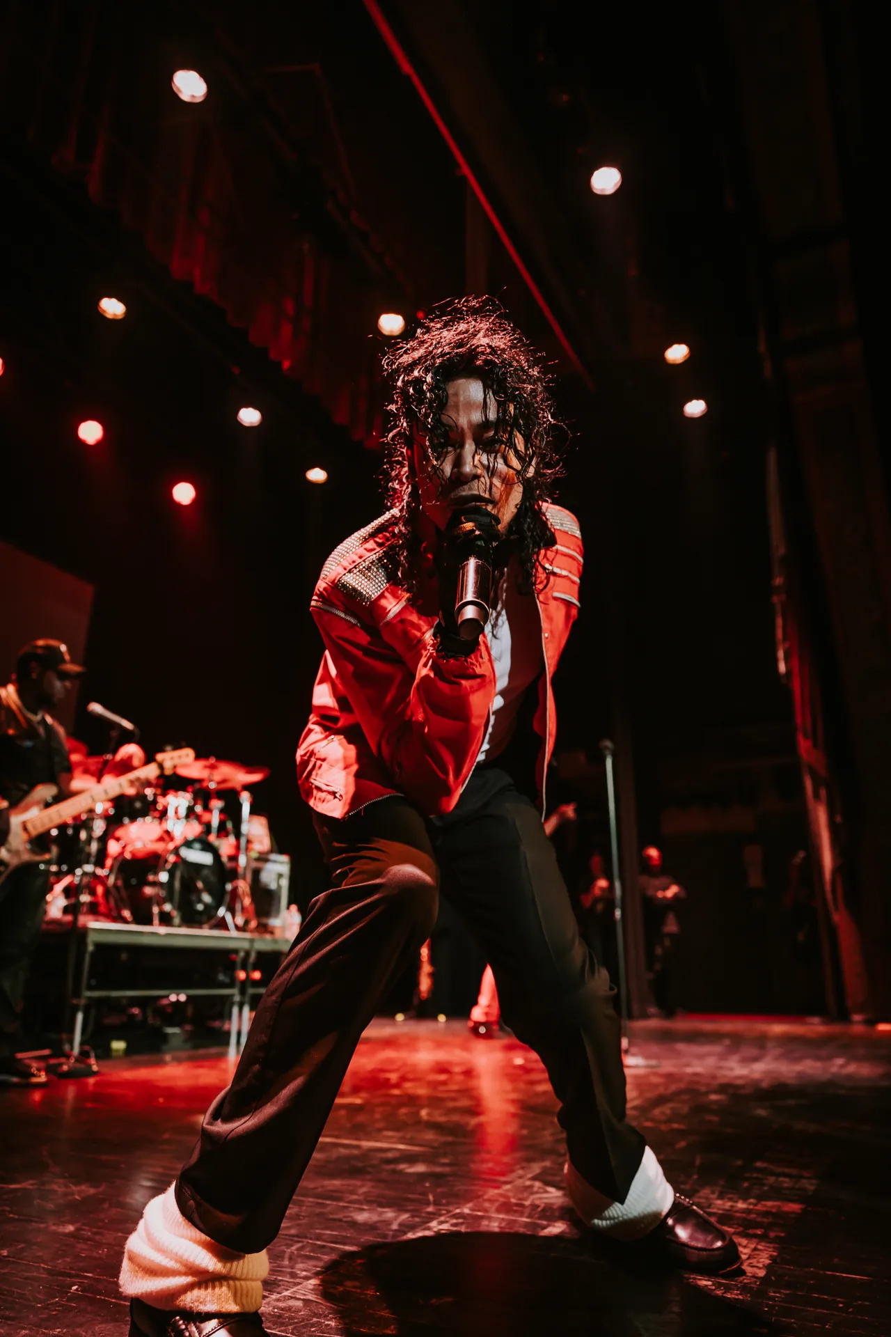 Who’s Bad performer in a red jacket strikes a wide-legged pose by the audience