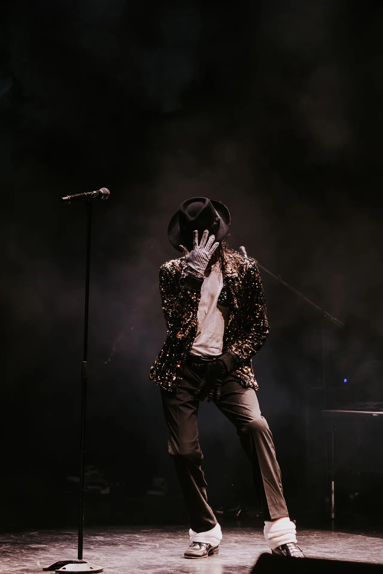 Who’s Bad performer in a black jacket and fedora dances alone in a spotlight